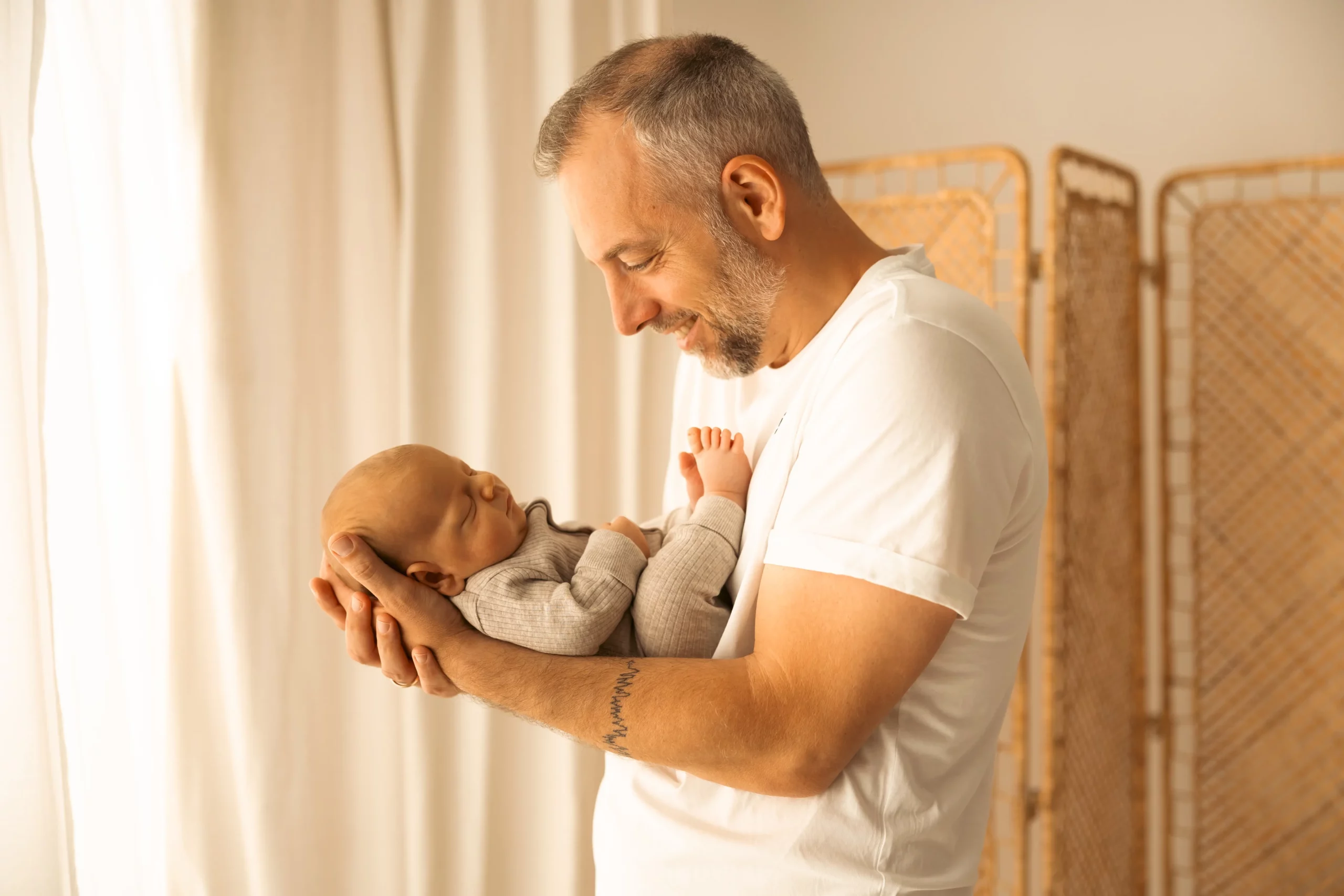 Vater blickt liebevoll auf sein Neugeborenes, das in seinen Armen ruhend im Fotostudio liegt.